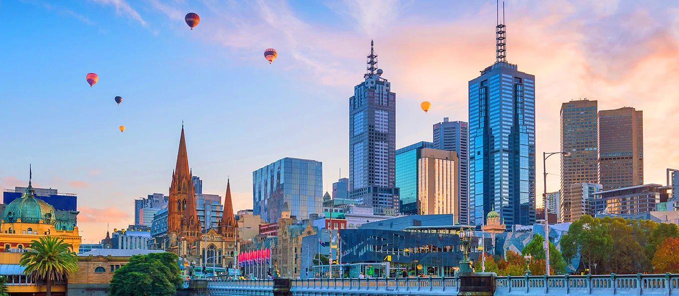 View of Melbourne city with skyscrapers, in the sunset with hot airballoons flating in the sky.
